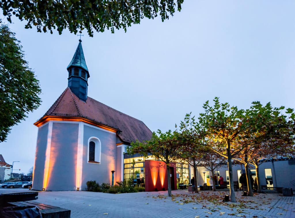 Die Spitalkirche wird in der Abenddämmerung von mehreren orangenen Strahlern beleuchtet.